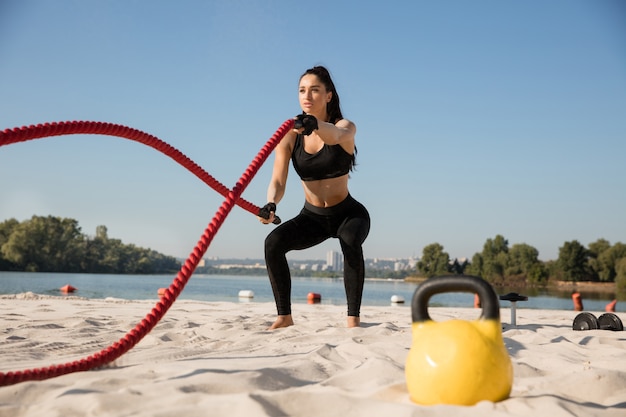 Junge gesunde Frau, die Übung mit den Seilen am Strand tut.