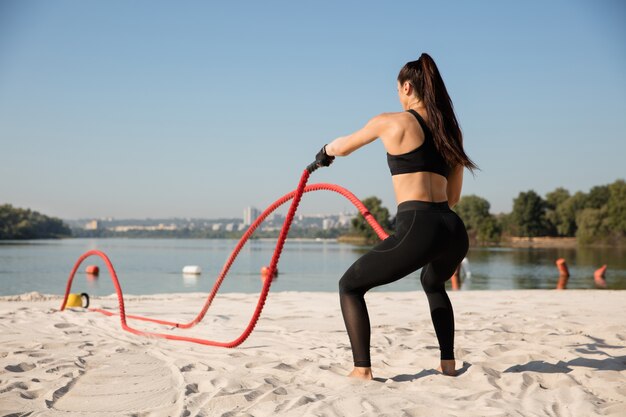 Junge gesunde Frau, die Übung mit den Seilen am Strand tut