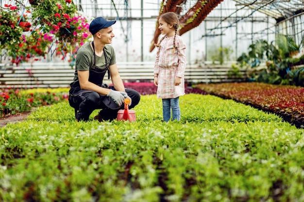 Junge Gewächshausarbeiterin spricht mit einem kleinen Mädchen, während sie Pflanzen nährt