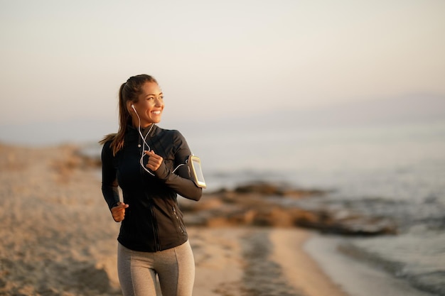 Junge glückliche athletische Frau, die sich beim Laufen am Strand motiviert fühlt Kopieren Sie Platz