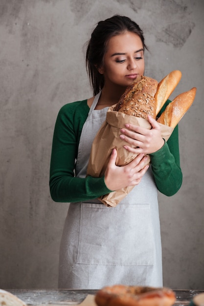 Junge glückliche Bäckerin stehend und hält Brot.