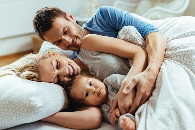 Junge glückliche Familie umarmt sich, während sie sich zusammen im Bett hinlegt.