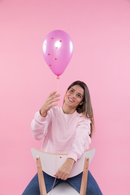 Junge glückliche Frau auf dem Stuhl, der violetten Ballon hält