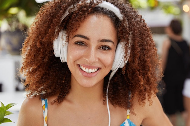 Junge glückliche Frau des Afroamerikaners genießt perfekten Klang, während Musik in modernen Kopfhörern hört
