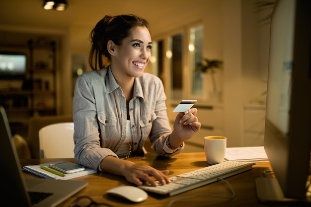 Junge glückliche Frau, die abends zu Hause Kreditkarte für Online-Shopping verwendet