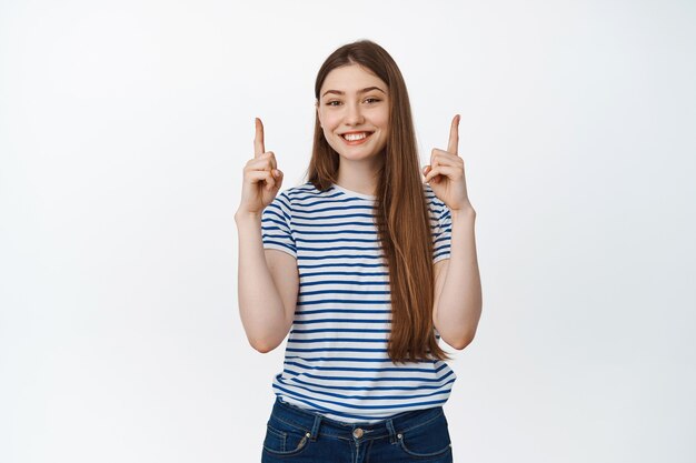Junge glückliche Frau, die Informationen zeigt, Finger nach oben zeigt und erfreut lächelt, Verkaufsfahne demonstriert, stehend auf Weiß.