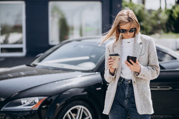 Junge glückliche Frau, die Kaffee durch das Auto trinkt