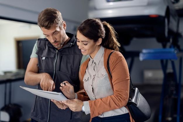 Junge glückliche Frau, die Papierkram in der Autowerkstatt unterschreibt