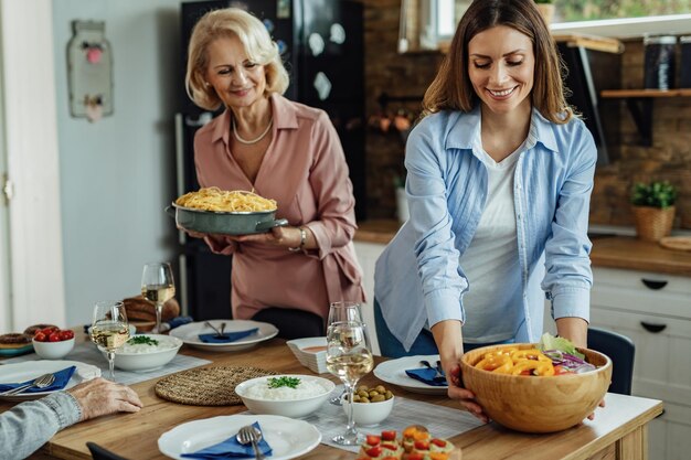 Junge glückliche Frau, die Salat serviert, während sie den Esstisch zum Mittagessen einstellt.