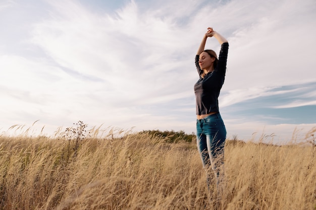 Junge glückliche Frau in einem goldenen Feld auf Sonnenuntergang.