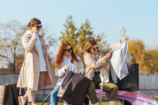 Junge glückliche Frauen mit Einkaufstaschen, die nahe einem alten verzierten Auto aufwerfen