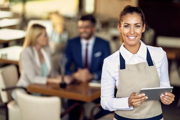 Junge glückliche Kellnerin mit Touchpad während der Arbeit in einem Café