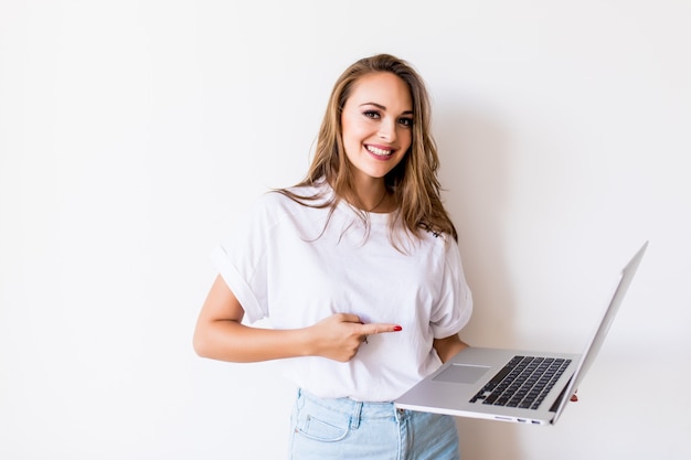 Junge glückliche lächelnde Frau in der Freizeitkleidung, die Laptop hält und E-Mail an ihren besten Freund sendet