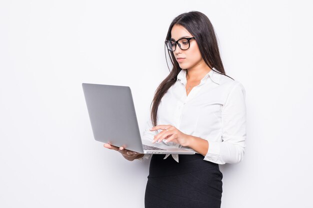 Junge glückliche lächelnde Geschäftsfrau in der Freizeitkleidung, die Laptop hält und E-Mail isoliert auf Weiß sendet