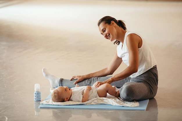 Junge glückliche Mutter, die ihre Beine streckt und Spaß mit ihrem kleinen Jungen hat, während sie im Fitnessstudio trainiert