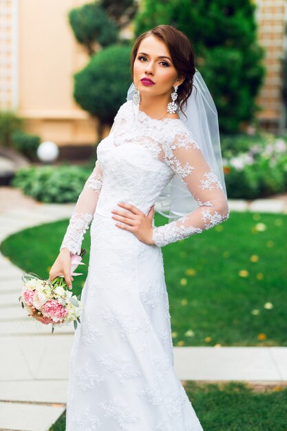 Junge glückliche schöne Braut im weißen eleganten Hochzeitskleid mit Blumenstrauß, der draußen im Park aufwirft.