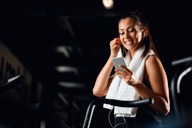 Junge glückliche Sportlerin benutzt Handy und hört Musik, während sie im Fitnesscenter trainiert Platz kopieren
