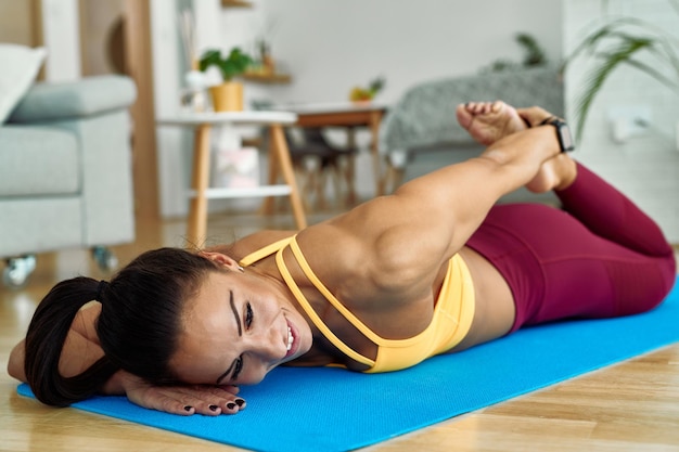 Junge glückliche Sportlerin, die Dehnübungen auf dem Boden im Wohnzimmer macht