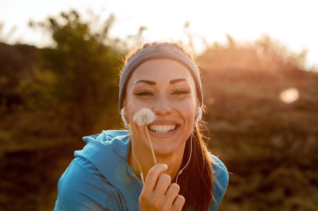 Junge glückliche Sportlerin, die Löwenzahnblume in der Natur hält und Kamera anschaut