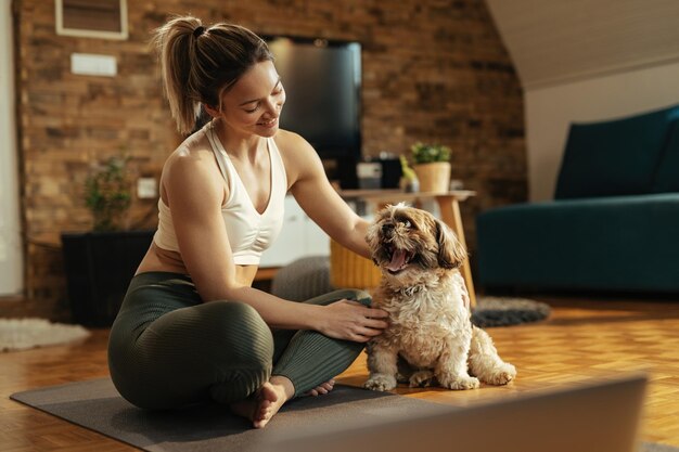 Junge glückliche Sportlerin genießt mit ihrem Hund, während sie sich zu Hause auf dem Boden entspannt