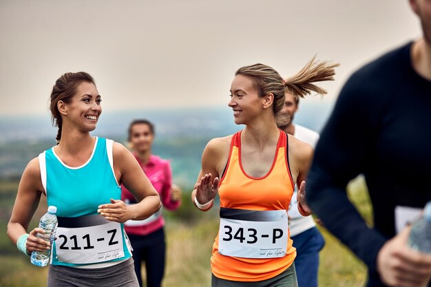 Junge glückliche Sportlerinnen, die an einem Marathon teilnehmen und während des Rennens kommunizieren