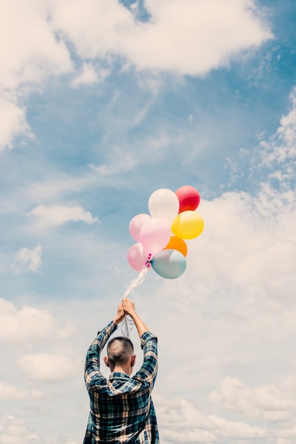 Kostenloses Foto junge hält bunten luftballons mit himmel im hintergrund