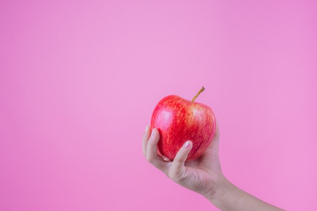 Junge hält und isst rote Äpfel auf einem rosa Hintergrund.