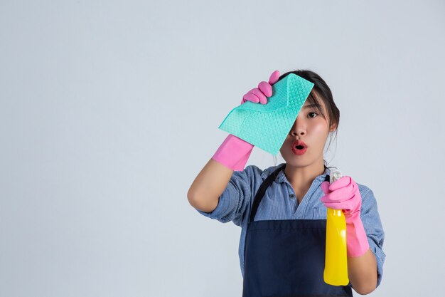 Junge Hausfrau trägt gelbe Handschuhe beim Putzen mit dem Produkt von sauber auf weißer Wand.