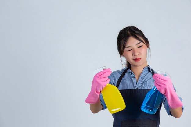 Junge Hausfrau trägt gelbe Handschuhe beim Putzen mit dem Produkt von sauber auf weißer Wand.