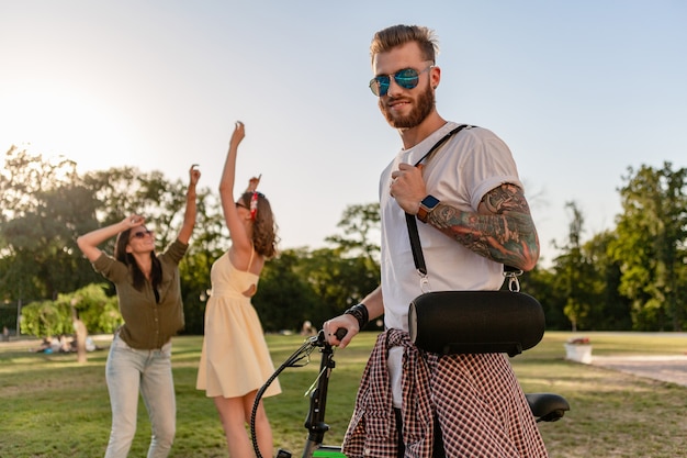 Junge Hipster-Firma von Freunden, die zusammen Spaß im Park haben und lächeln, Musik auf drahtlosen Lautsprechern hören?