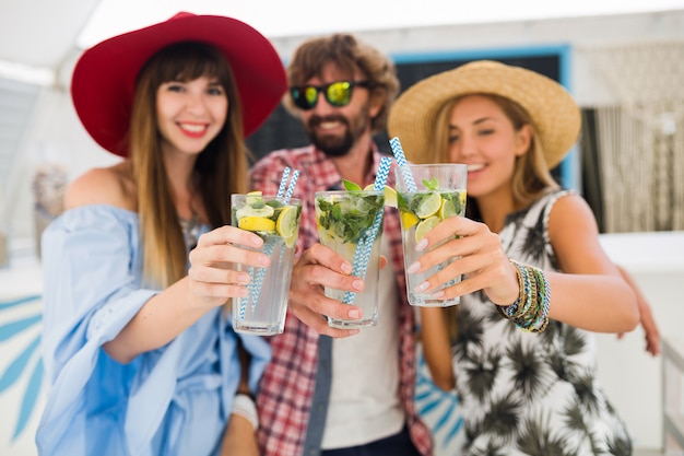 Kostenloses Foto junge hipster-gesellschaft von freunden im urlaub im sommercafé, mojito-cocktails trinkend, glücklicher positiver stil, glücklich lächelnd, zwei frauen und mann, die spaß zusammen haben, reden, flirten, romantik, drei