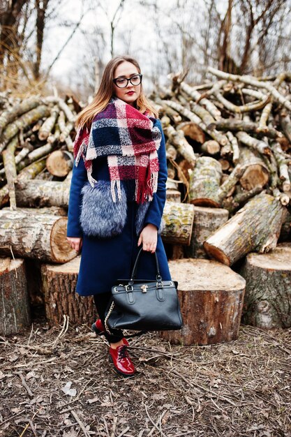 Junge Hipster-Mädchen tragen Mantel und Schal mit Handtasche gegen Holzstümpfe auf Holz