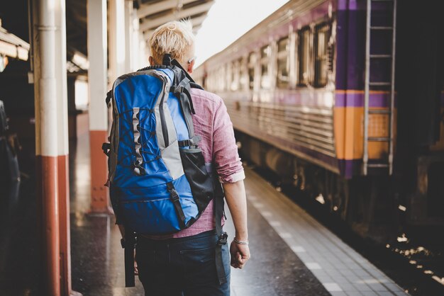 Junge Hipster Tourist mit Rucksack auf dem Bahnhof. Urlaubstourismuskonzept.