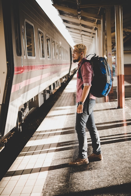 Junge Hipster Tourist mit Rucksack auf dem Bahnhof. Urlaubstourismuskonzept.