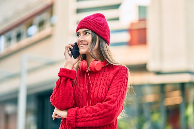 Junge hispanische Frau, die auf dem Smartphone mit Kopfhörern in der Stadt spricht.