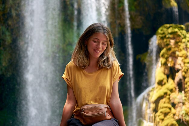 Junge hispanische Frau lächelt mit geschlossenen Augen mit einem Wasserfall im Hintergrund