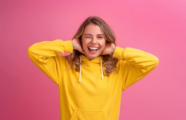 Junge hübsche blonde Frau süßer Gesichtsausdruck posiert in gelbem Hoodie auf rosa hellem Hintergrund isoliert emotional lustig