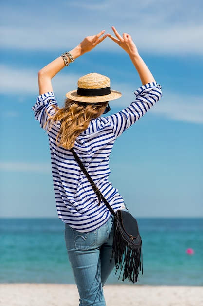 Junge hübsche blonde gebräunte junge frau, die am strand nahe dem meer zurück wartet und träumt