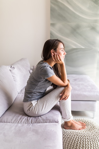 Junge hübsche Frau, die auf der Couch sitzt und denkt