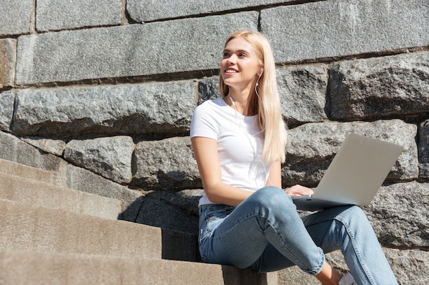 Junge hübsche Frau, die auf Treppe mit Laptop-Computer sitzt