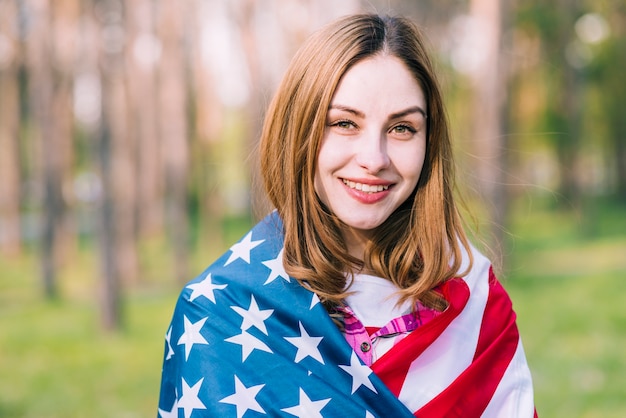 Junge hübsche Frau, die draußen in USA-Flagge einwickelt