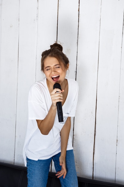 Junge hübsche Frau, die im Mikrofon auf Sofa zu Hause singt.