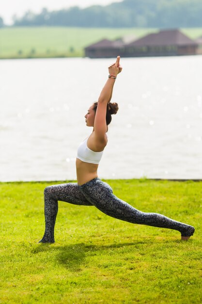 Junge hübsche Frau, die Yoga im Morgenpark nahe See tut