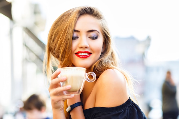 Junge hübsche Frau genießt, trinkt Tasse Cappuccino, Latte, Kaffee im Morgenstraßencafé.
