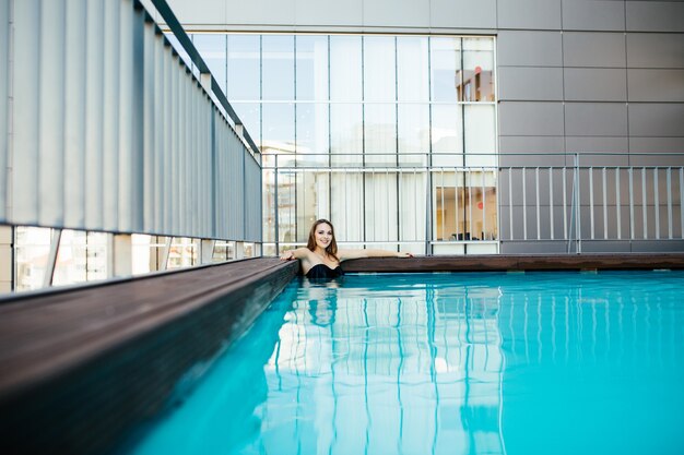 Junge hübsche Frau im schwarzen Badeanzug entspannt sich am Rand des Pools
