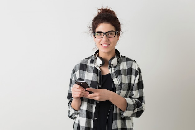 Junge hübsche Frau in der Brille, Smartphone haltend, mit digitalem Gerät, lächelnd, glücklich, Kopfhörer, isoliert, kariertes Hemd, Student, schauend