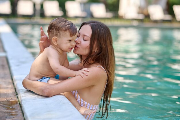 Junge hübsche Frau in einem Swimmingpool, die ihren kleinen Jungen küsst