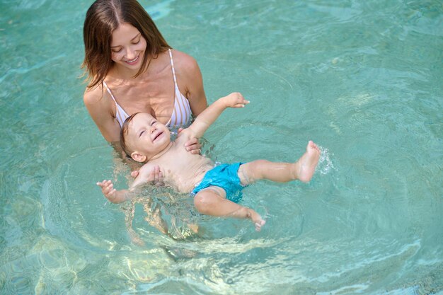 Junge hübsche Frau in einem Swimmingpool mit ihrem kleinen Jungen