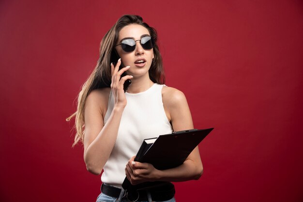 Junge hübsche Frau mit Brille, die am Telefon spricht und Notizbücher hält