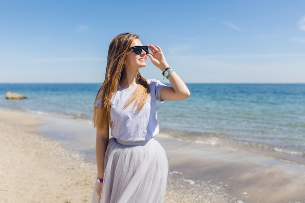 Junge hübsche Frau mit langen Haaren geht auf dem Strand nahe Meer